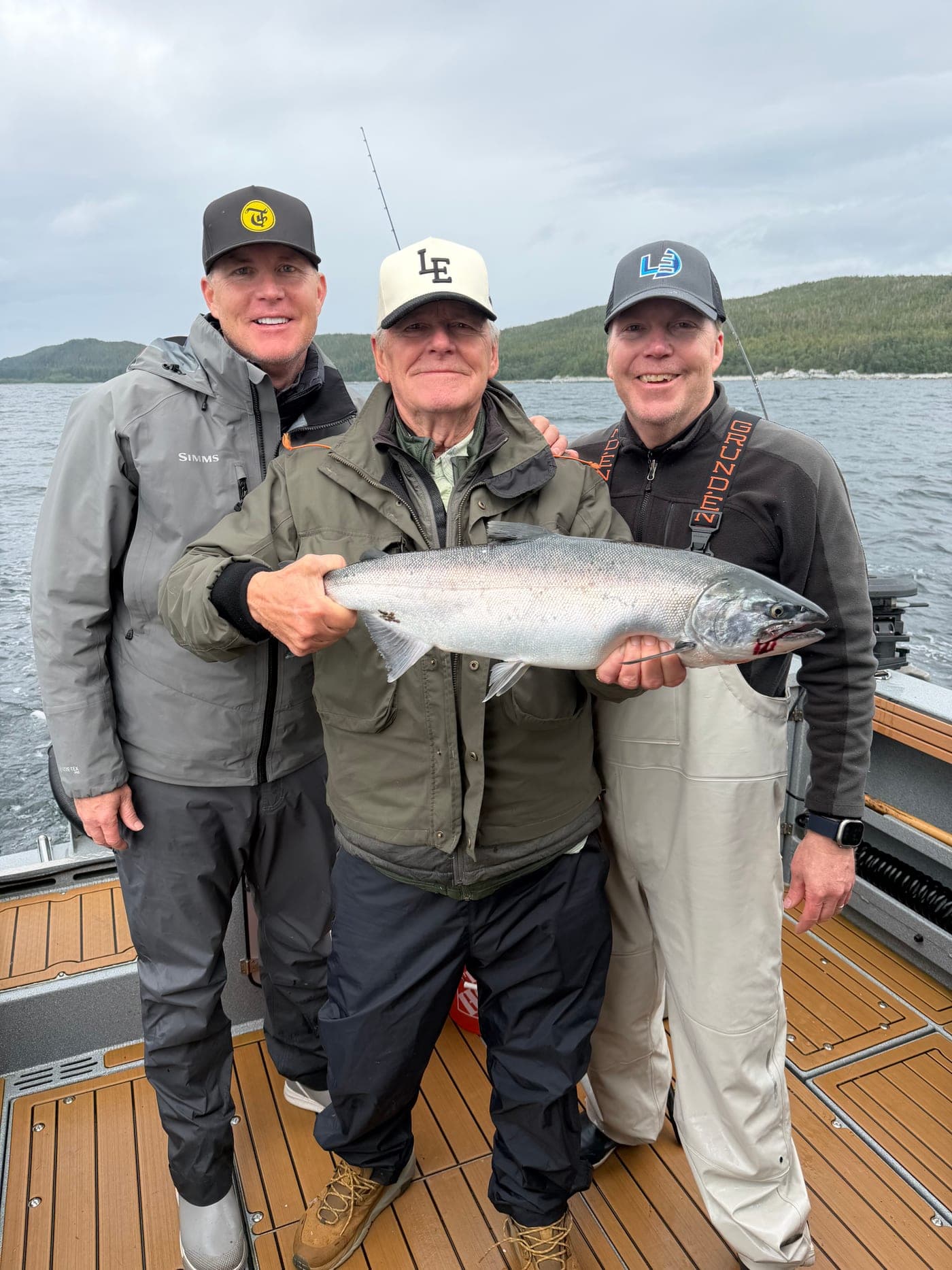 Garth Williams on a boat holding a salmon, flanked by two fishing companions